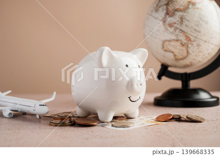 Hand putting coin into piggy bank with airplane and globe, travel savings budget planning and vacation finance concept Hand putting coin into piggy bank with airplane and globe, travel savings budget planning and vacation finance concept 139668335