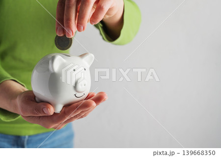 Person putting coin into piggy bank, savings personal finance budgeting and financial growth concept Person putting coin into piggy bank, savings personal finance budgeting and financial growth concept 139668350