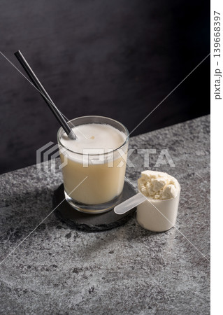 Protein vanilla shake in drinking glass and scoop with whey protein powder on dark background Protein vanilla shake in drinking glass and scoop with whey protein powder on dark background 139668397