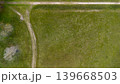 Top down aerial view of a green meadow with a dirt path intersection and a lonely bench. Minimalist rural landscape captured from above, showcasing texture, geometry, and peaceful countryside. 139668503