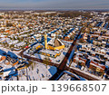 Aerial view of a snow-covered Dutch town with a modern church building and residential houses under a clear blue sky. Winter landscape in the Netherlands with snowy rooftops and streets. 139668507