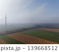 Aerial perspective of multiple wind turbines stretching into a misty, agricultural landscape on a clear, high-altitude morning. Sustainable green energy farm concept. 139668512