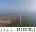 Aerial view of a wind turbine standing in a green field during a foggy morning. Sustainable energy and eco-friendly technology in a rural European landscape with hazy horizon. 139668513