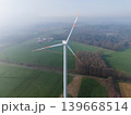 Aerial perspective of multiple wind turbines stretching into a misty, agricultural landscape on a clear, high-altitude morning. Sustainable green energy farm concept. 139668514
