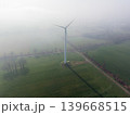 Aerial view of a solitary wind turbine standing in vast green agricultural fields on a foggy, misty morning. Clean energy technology in a rural environment. 139668515
