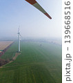 Aerial view looking through the rotating blade of a wind turbine, showing a single turbine standing in a misty, agricultural landscape. Sustainable green energy concept in fog. 139668516