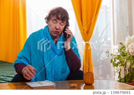 Older Caucasian woman playing dice game at home and calls on phone. Calm environment and focus. Concept of hobby and relaxation. 139670691