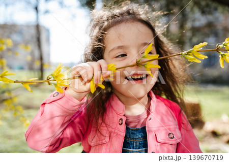 Caucasian girl holding blooming forsythia branch with yellow flowers in sunny park area. Childhood and spring lifestyle Caucasian girl holding blooming forsythia branch with yellow flowers in sunny park area. Childhood and spring lifestyle 139670719