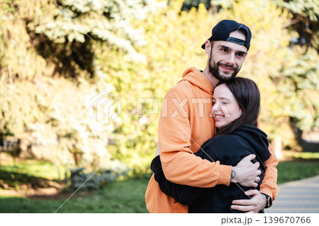 Caucasian husband and wife hugging together in sunny park with trees in blurred background outdoors. Marriage and relationship lifestyle Caucasian husband and wife hugging together in sunny park with trees in blurred background outdoors. Marriage and relationship lifestyle 139670766
