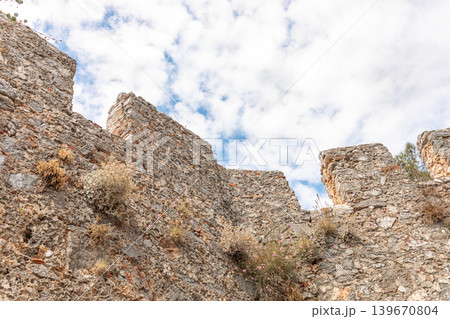 Bottom view to ancient stone wall ruins under cloudy sky with vegetation visible Bottom view to ancient stone wall ruins under cloudy sky with vegetation visible 139670804