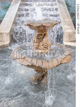 Ornate stone fountain with cascading water in urban park setting 139670815