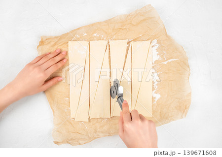 Cutting croissant dough into triangles on baking paper, top view pastry preparation Cutting croissant dough into triangles on baking paper, top view pastry preparation 139671608