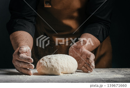 Professional baker shaping fresh dough by hand on dark background for artisan bread and bakery advertising concept Professional baker shaping fresh dough by hand on dark background for artisan bread and bakery advertising concept 139671660