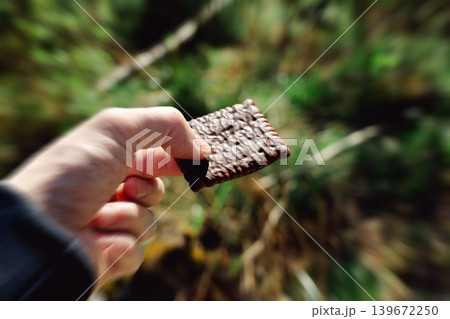 Man holding chocolate biscuit in forest. Outdoor snack break with blurred green nature background, food and relaxation concept Man holding chocolate biscuit in forest. Outdoor snack break with blurred green nature background, food and relaxation concept 139672250