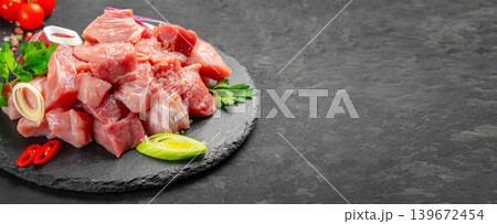 Raw diced pork meat with herbs and spices on slate plate over dark background copy space Raw diced pork meat with herbs and spices on slate plate over dark background copy space 139672454