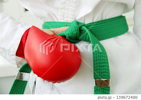 A close-up of a martial artist in a white kimono with a green striped belt. The karateka holds his belt with his hand. Conceptually, it represents strength, discipline, and combat sports 139672480
