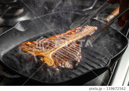 Grilled t-bone steak with tongs on hot pan, smoke and sear marks Grilled t-bone steak with tongs on hot pan, smoke and sear marks 139672562