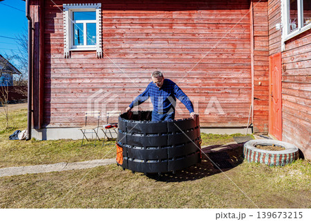 Gardener setting up compost bin by connecting plastic sections outdoors. Gardener setting up compost bin by connecting plastic sections outdoors. 139673215