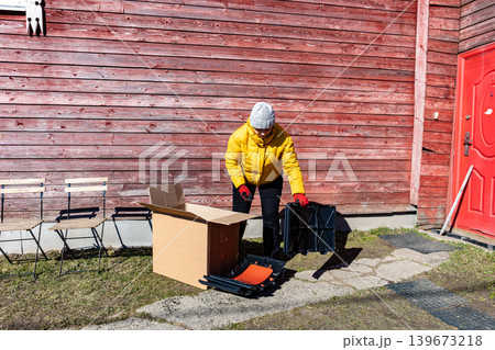 Gardener taking compost bin components and plastic sections out of shipping box outdoors. Gardener taking compost bin components and plastic sections out of shipping box outdoors. 139673218