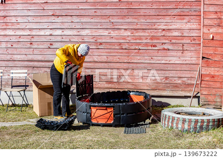 Assembling modular composter from plastic panels female gardener inserts sections into grooves with latch lock Assembling modular composter from plastic panels female gardener inserts sections into grooves with latch lock 139673222