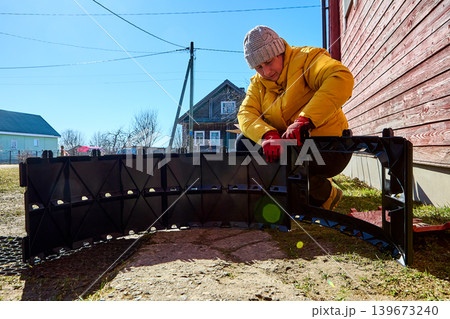 Large segmented compost section being connected with stackable plastic components by rural woman during outdoor assembly process. Large segmented compost section being connected with stackable plastic components by rural woman during outdoor assembly process. 139673240