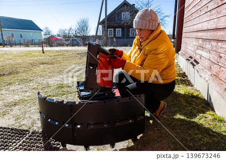 Female homeowner connecting modular plastic panels for compost bin assembly beside open cardboard box. 139673246