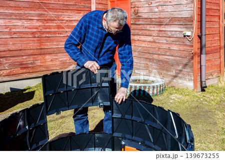 Installation modular compost bin with interlocking panels, farmer assembles parts by inserting one into other and clicking them together. 139673255