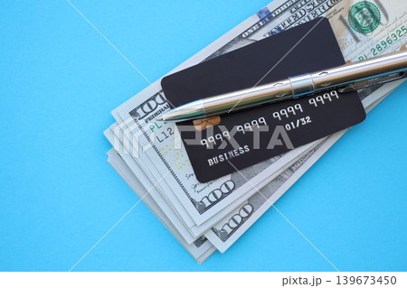 Credit card and pen with US dollar currency money bills banknotes on light blue background 139673450