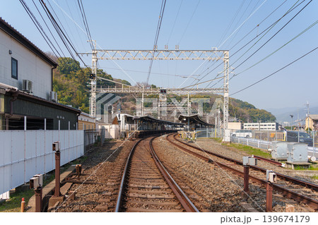 Railway track lead into countryside platform station with overhead electric wire and forested hill in suburban Railway track lead into countryside platform station with overhead electric wire and forested hill in suburban 139674179