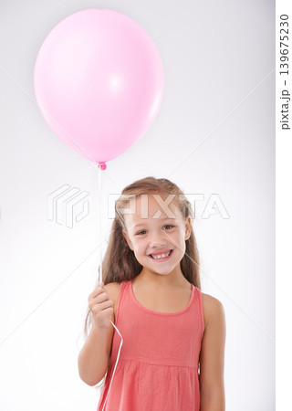 Girl, child and balloon in portrait, party decoration and smiling for milestone event in studio. Happy female person, inflatable accessory and birthday joy on white background, playful and celebrate 139675230