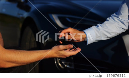 Male hand giving key of car to buyer of electric automobile outdoor. Handshake between salesman and new owner of modern auto after successful deal. Concept of buy or rent car. Slow mo 139676311