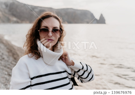 Woman seascape fashion portrait of elegant lady in striped sweater and sunglasses standing on rocky coast with cliffs and copy space 139676976