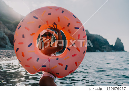 Young woman donut float ocean smiles through inflatable donut on summer vacation with copy space. 139676987