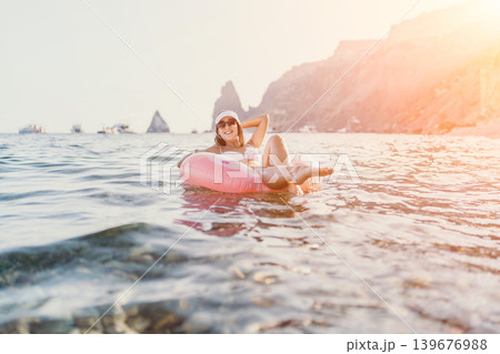 Woman, ocean, relaxation, happy female enjoying summer vacation on pink inflatable ring in serene sea with cliffs. 139676988