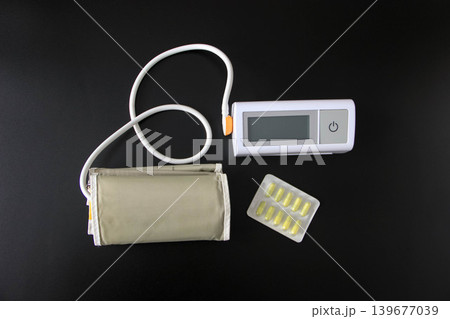 Digital blood pressure monitor with cuff and pills on black background 139677039