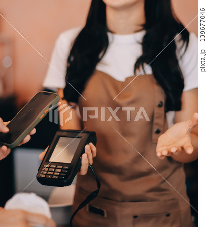 Asian senior female barista adult receiving mobile payment from customer using smartphone at cafe demonstrating modern cashless transaction in cozy local family coffee shop 139677046