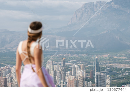 Woman in sportswear gazing at mountain landscape over city skyline Woman in sportswear gazing at mountain landscape over city skyline 139677444