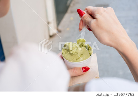 Woman enjoying matcha ice cream with red nails on a sunny day outdoors 139677762