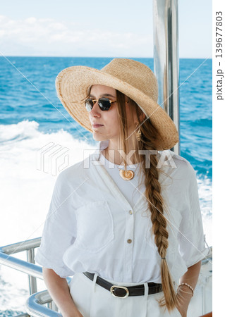 Stylish woman in sun hat and sunglasses relaxing on a boat at sea Stylish woman in sun hat and sunglasses relaxing on a boat at sea 139677803