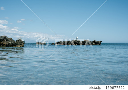 Serene rocky shoreline overlooking calm ocean with blue sky horizon Serene rocky shoreline overlooking calm ocean with blue sky horizon 139677822