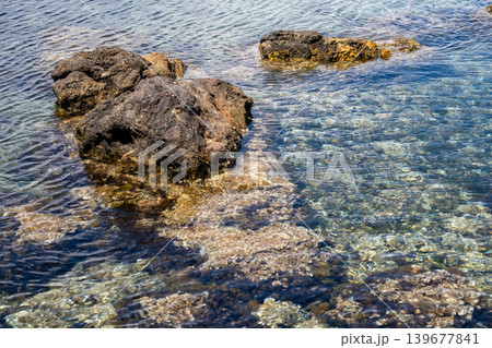 Clear ocean water flowing over rocks at a sunlit beach 139677841