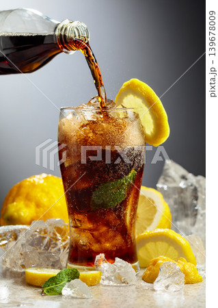 Cola is poured from a bottle into a misted glass with lemon slices, ice and mint. Cola is poured from a bottle into a misted glass with lemon slices, ice and mint. 139678009