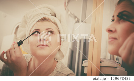 Woman in bathroom applying mascara on eyelashes 139678482