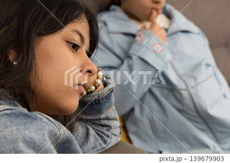 A teenager is sitting on a couch with her head down A teenager is sitting on a couch with her head down 139679903