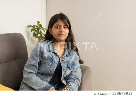 A teenager is sitting on a couch wearing a blue jacket A teenager is sitting on a couch wearing a blue jacket 139679912
