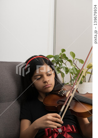 A young girl is playing the violin in a living room A young girl is playing the violin in a living room 139679934