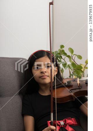 A young girl is sitting on a couch holding a violin A young girl is sitting on a couch holding a violin 139679935