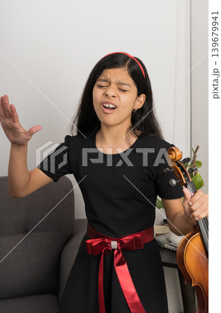 A young girl in a black dress is playing a violin 139679941