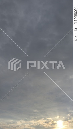 A vertical image showing a cloudy sky at sunrise, with the sun's light shining brightly through the clouds at the bottom. A vertical image showing a cloudy sky at sunrise, with the sun's light shining brightly through the clouds at the bottom. 139680644