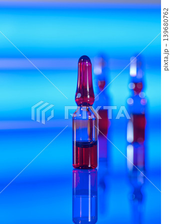 Colorful glass ampoules stand on a reflective surface with a blue background in a modern setting during daytime Colorful glass ampoules stand on a reflective surface with a blue background in a modern setting during daytime 139680762